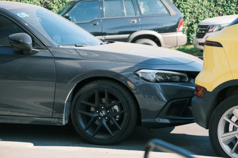 Dark grey sedan damaged from a rear-end collision with a yellow vehicle.